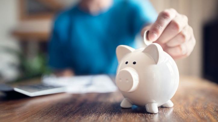 A person drops a coin in a piggy bank as a symbol of saving for retirement.