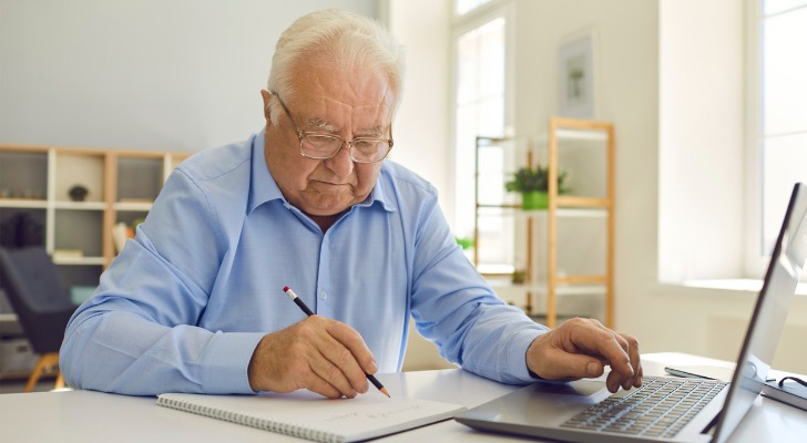 A man jots in a notebook while using a laptop computer. 