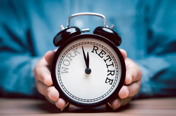 A businessman holding a black alarm clock with clockwise countdown from work to retirement.
